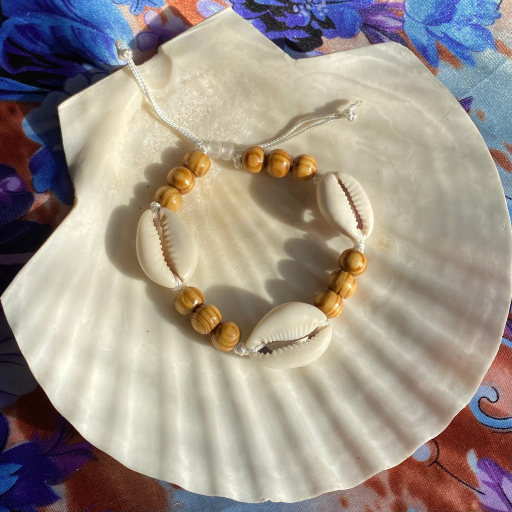 Adjustable bracelet made with light brown wood beads and white cowrie shells.