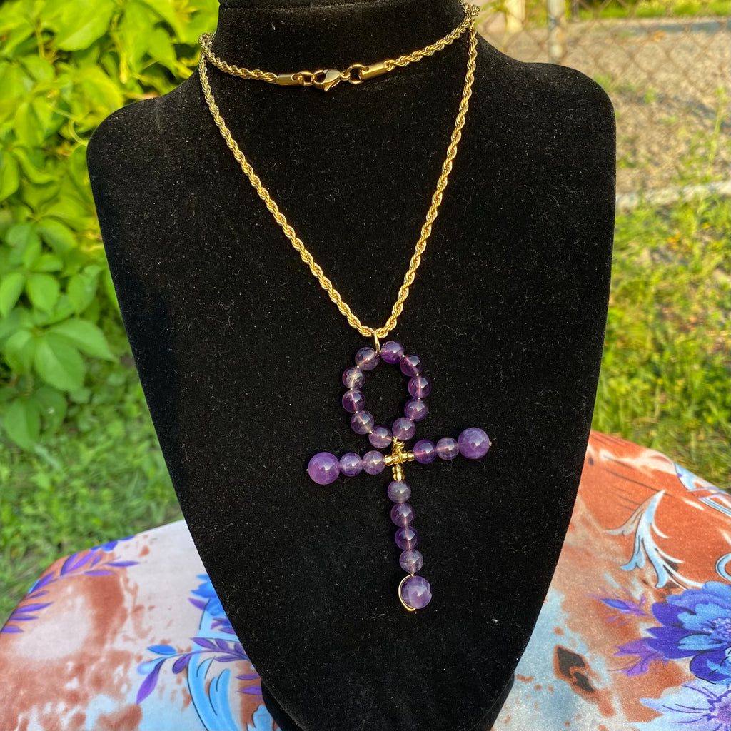 A necklace with a gold chain and a purple amethyst beaded ankh pendant.