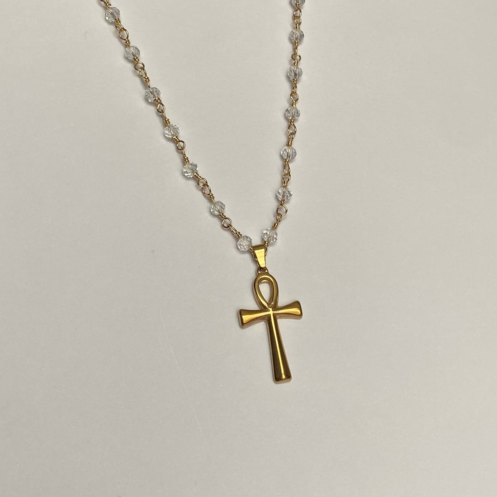 Necklace with gold colored ankh pendant on a clear beaded chain with gold colored links.