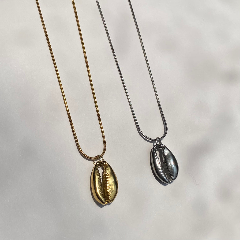 Two cowrie shell-shaped pendants on gold and silver necklaces displayed on a light background