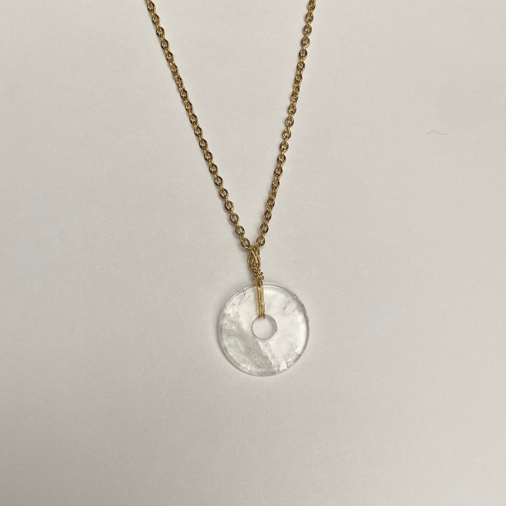 a necklace layed out on a flat surface, gold toned chain with clear quartz disc pendant.