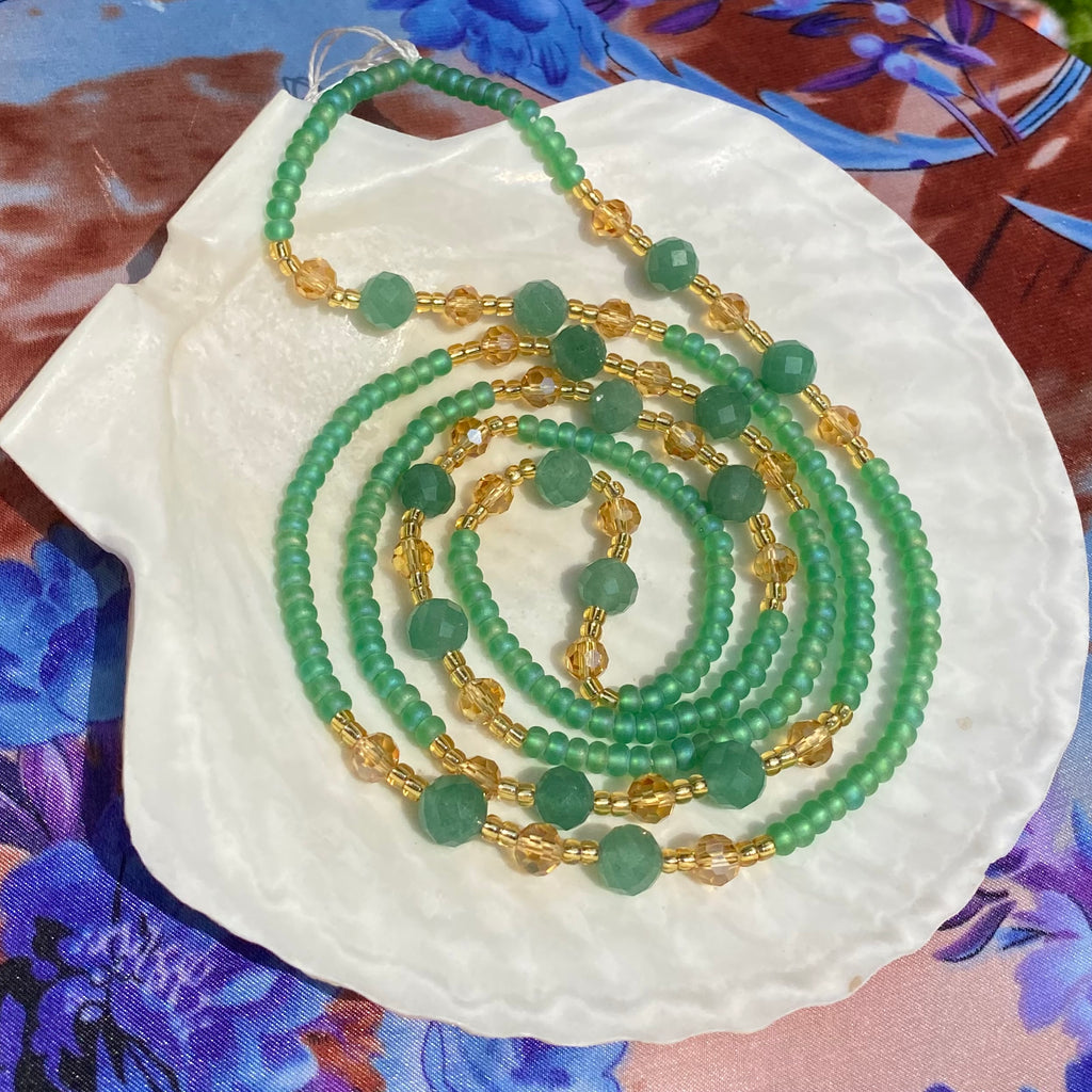 green and gold waist beads with facetted aventurine stone displayed on a white shell.