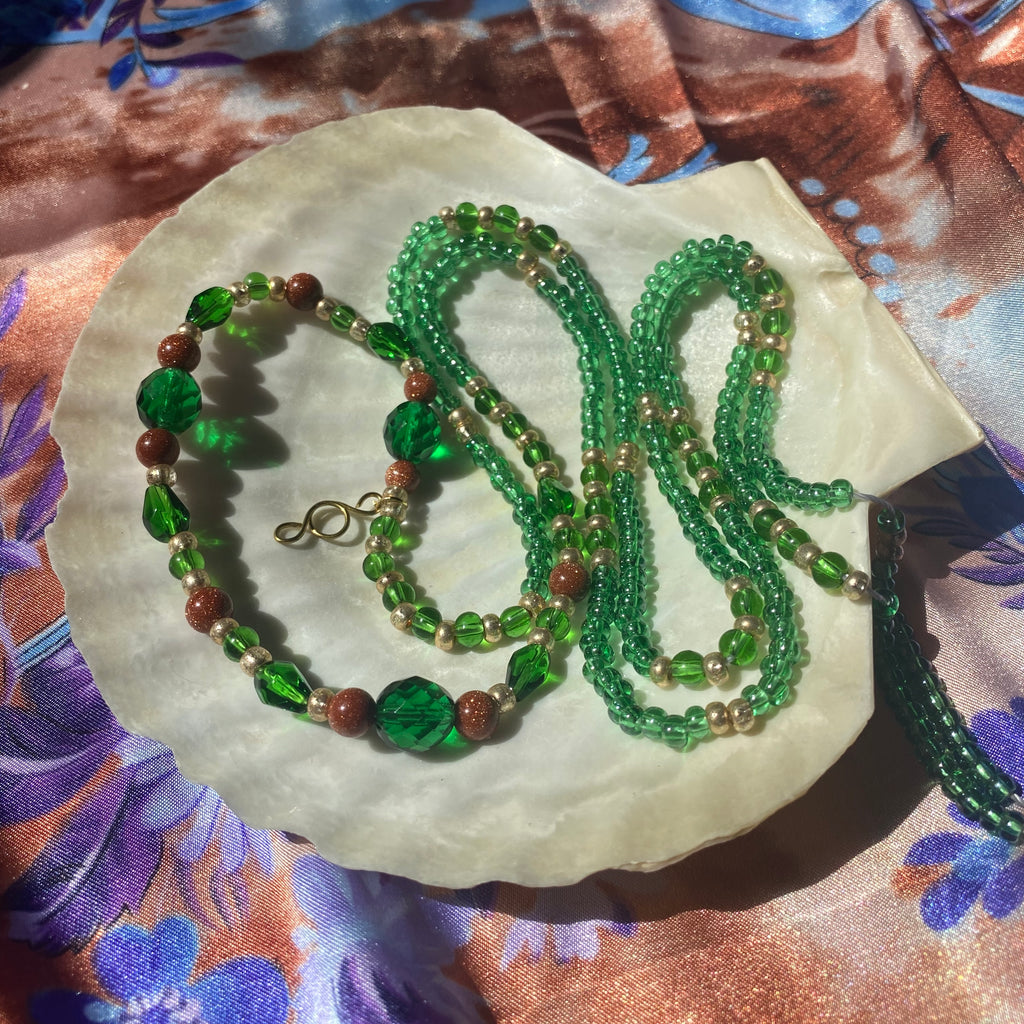 Green waist beads with goldstone crystal and a gold pendant presented on a shell.