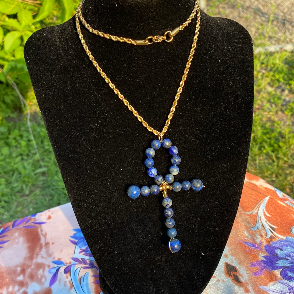 A black mannequin wearing a gold-colored chain necklace with an Ankh pendant made of blue lapis lazuli beads.
