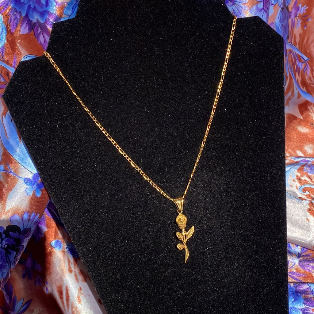A stainless steel necklace with a rose pendant displayed on an 18-inch chain, presented on a black mannequin against a floral background.