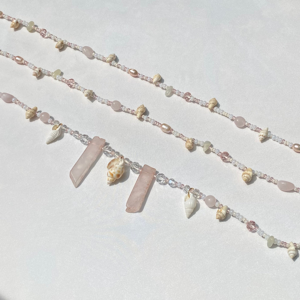 pink and white waist beads with shells and rose quartz charms on a white background.